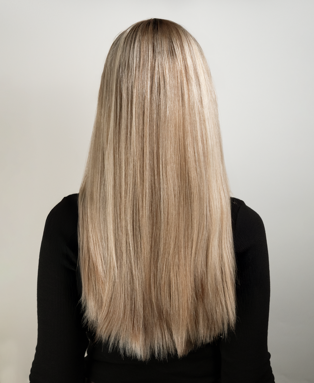 Person with long, straight blonde hair wig wearing a black top on a plain background