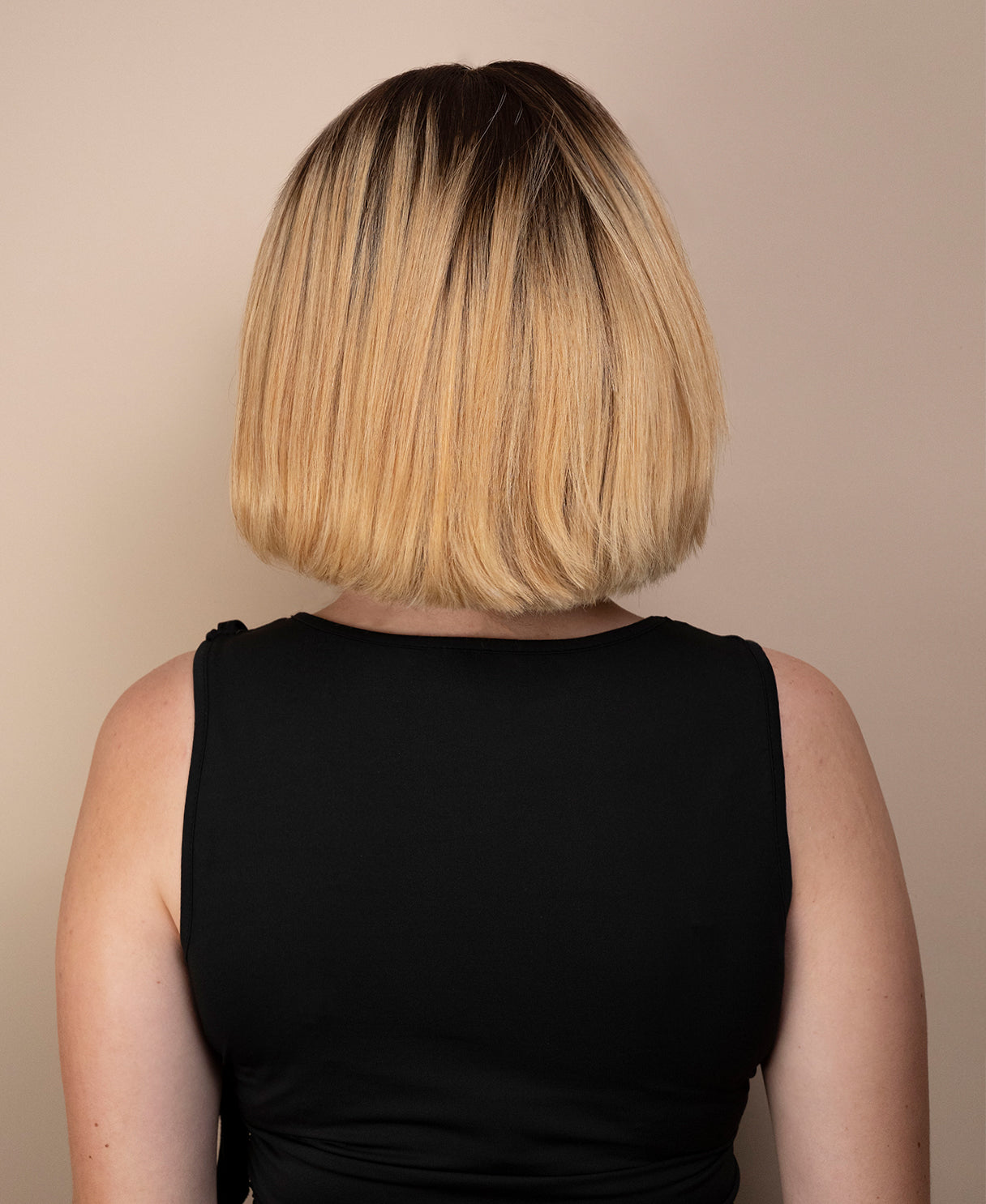 Person with a short, blonde ombre bob wig haircut against a beige background
