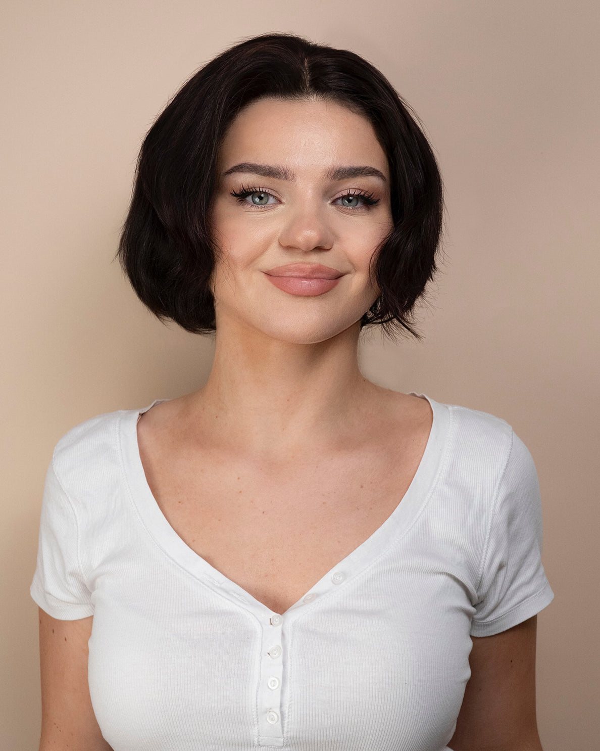 Woman wearing a black hair wig and white shirt against a beige background