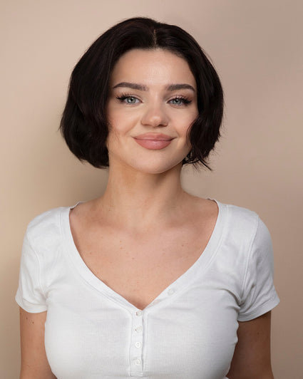 Woman wearing a black hair wig and white shirt against a beige background