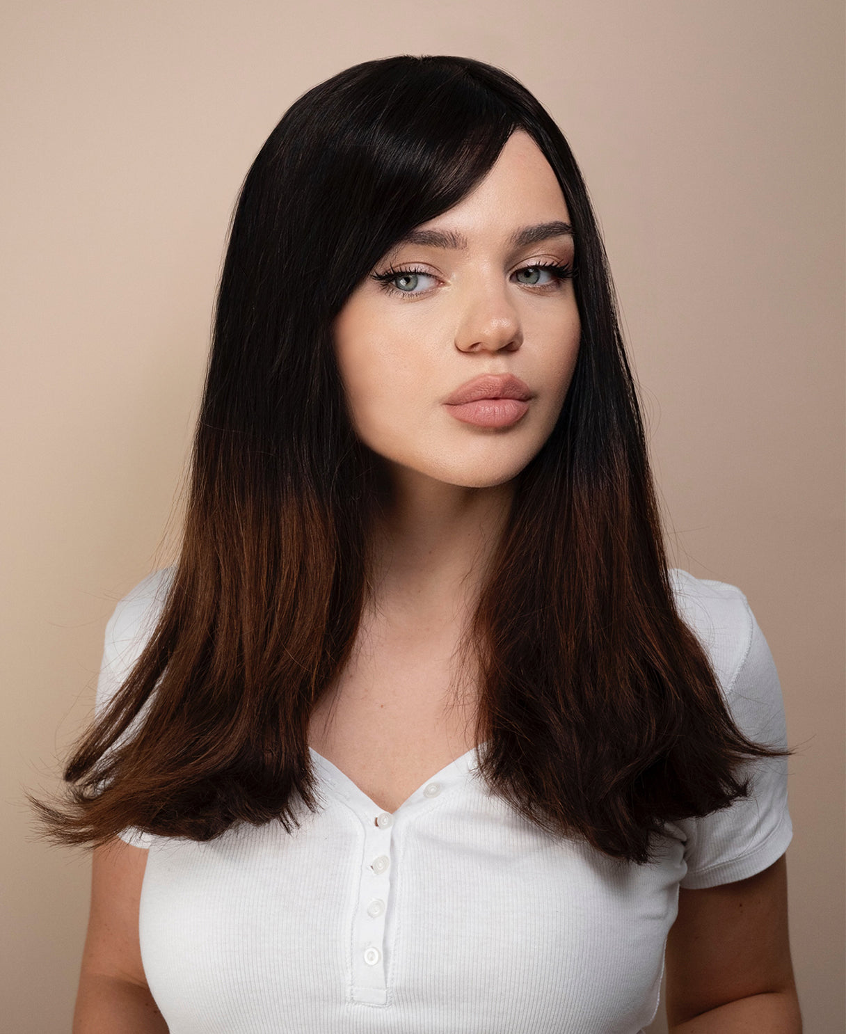 Woman with long dark hair wig wearing a white shirt against a beige background