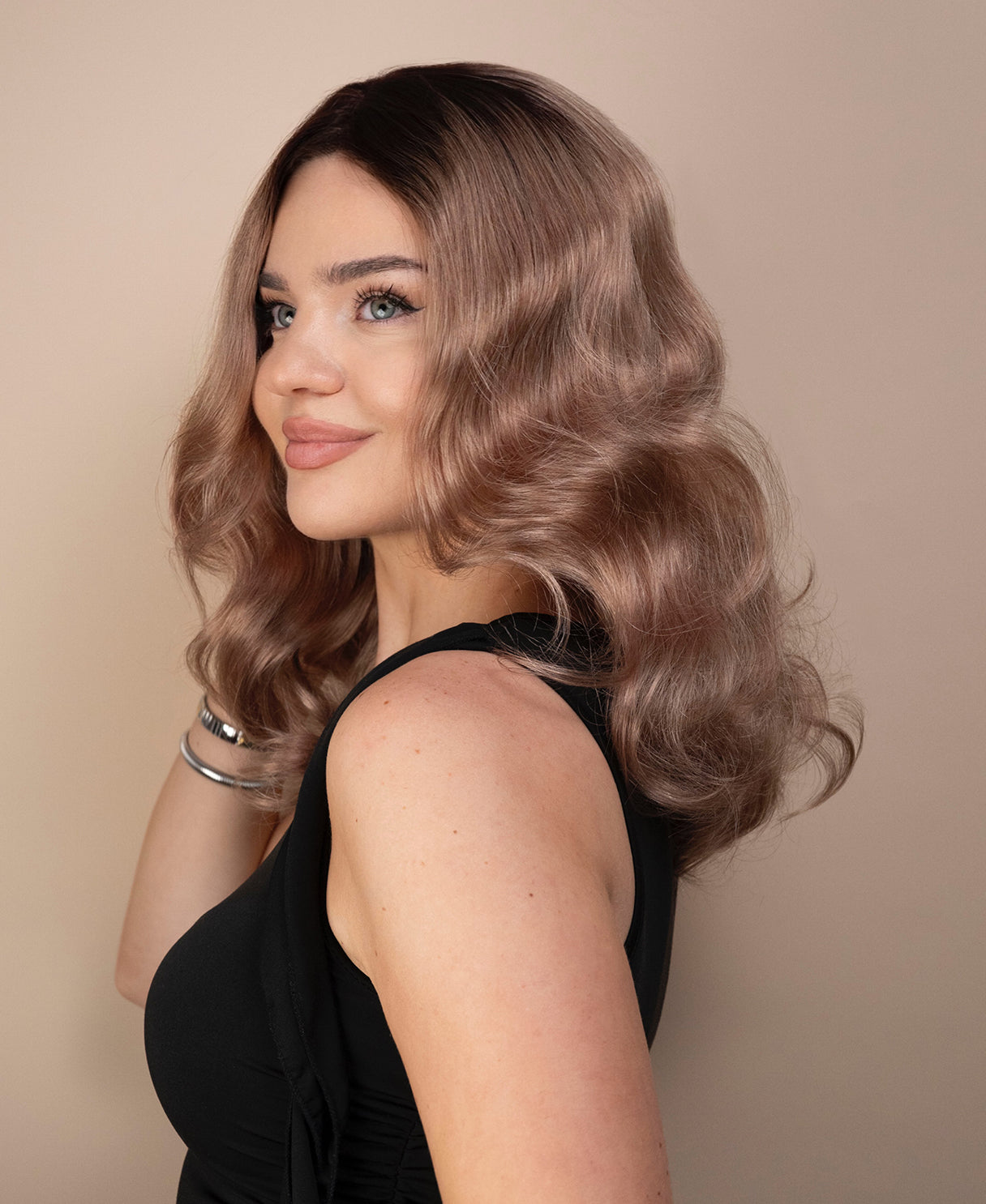 Woman with wavy ash wig wearing a black top against a beige background