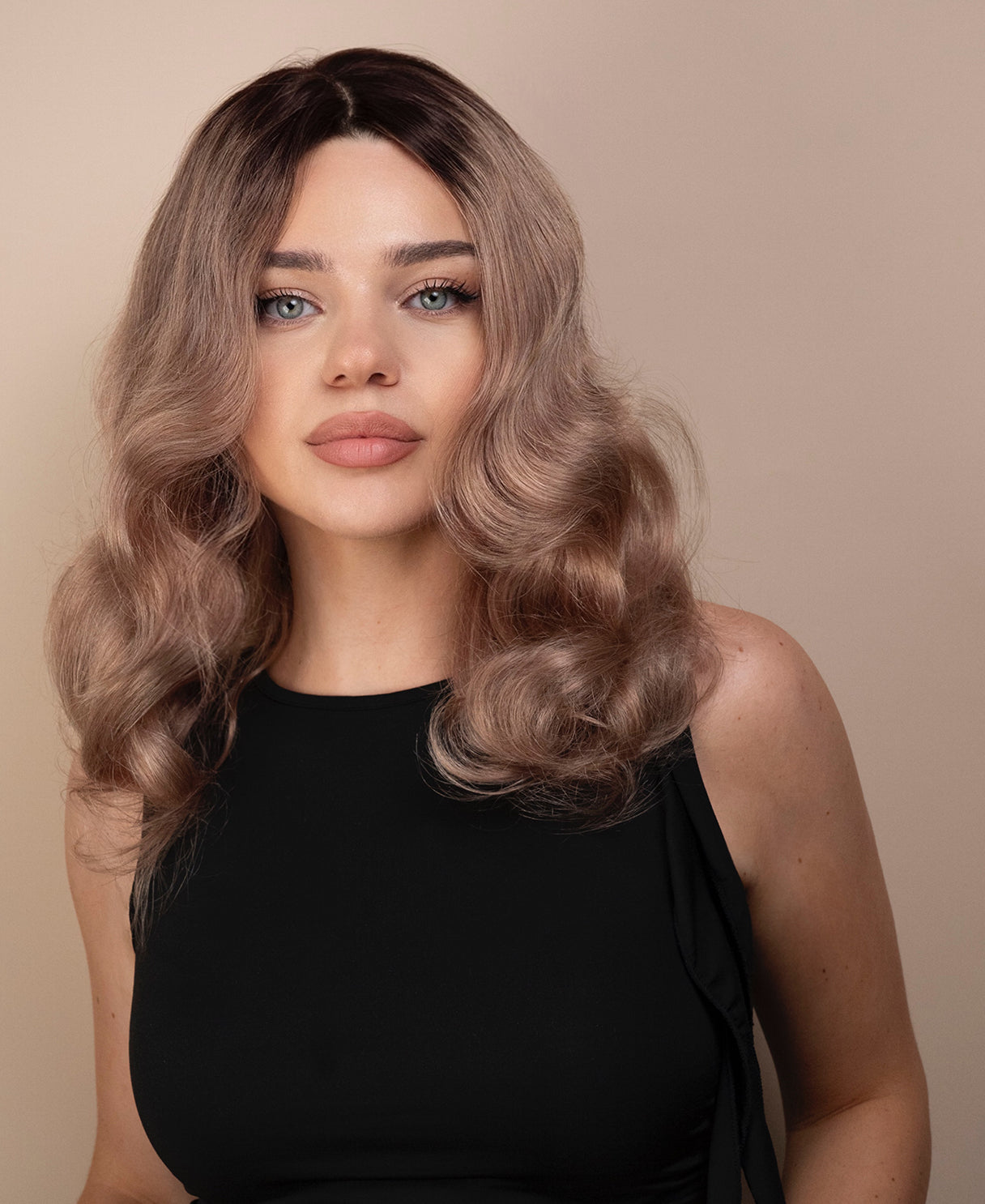 Woman with wavy ash wig wearing a black top against a beige background