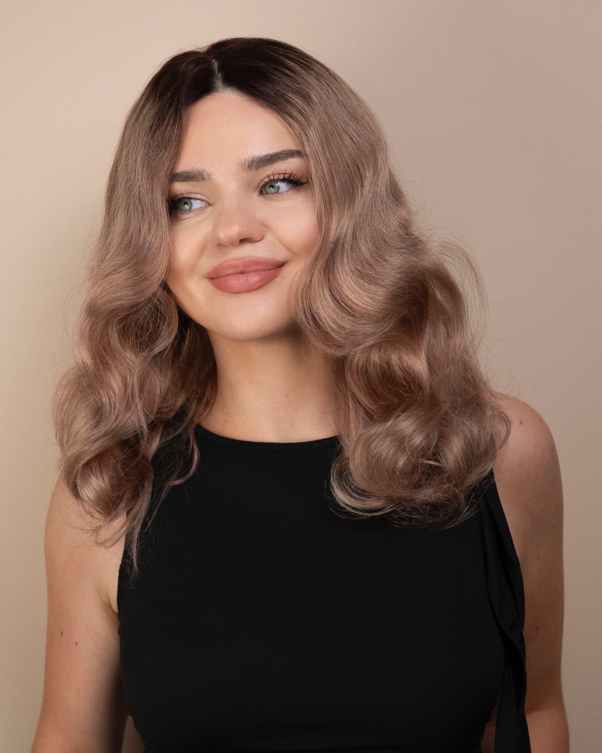 Woman with wavy ash wig wearing a black top against a beige background