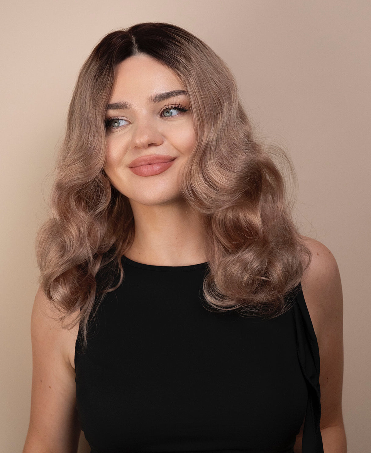 Woman with wavy ash wig wearing a black top against a beige background