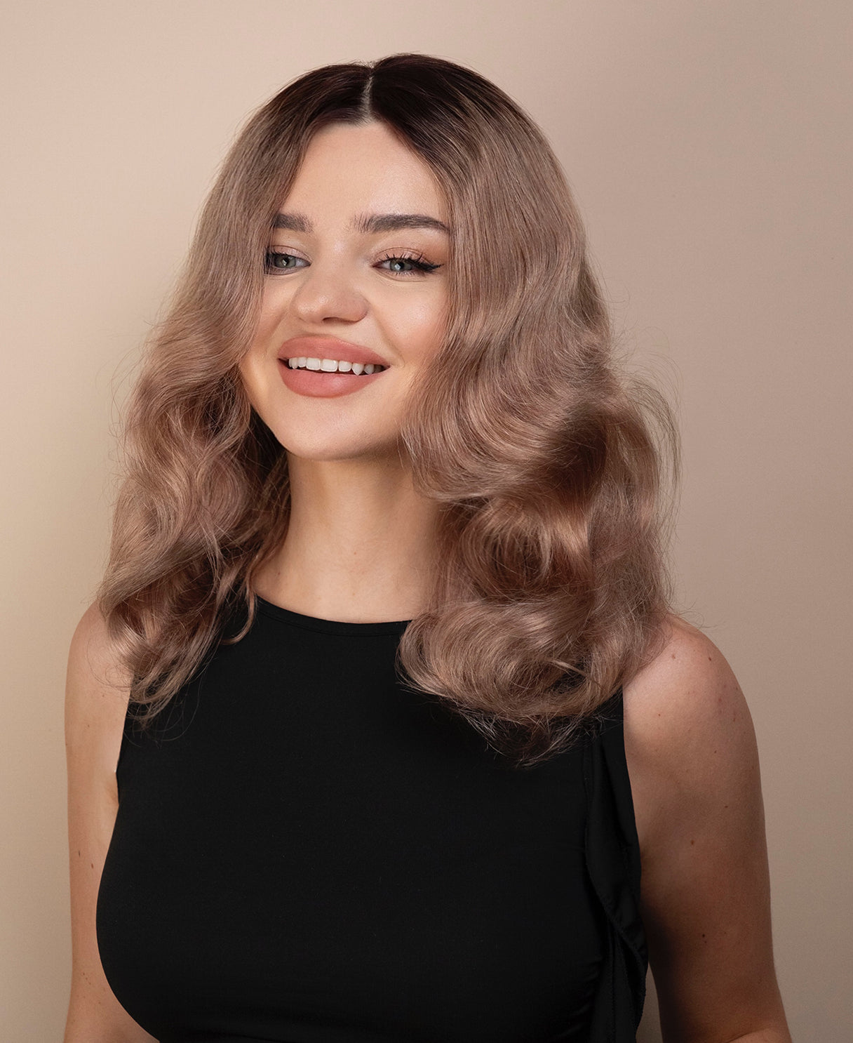 Woman with wavy ash wig wearing a black top against a beige background