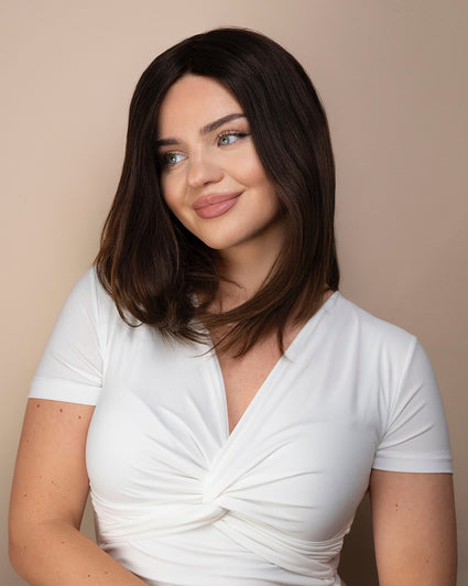 Woman wearing a a brown wig against a beige background