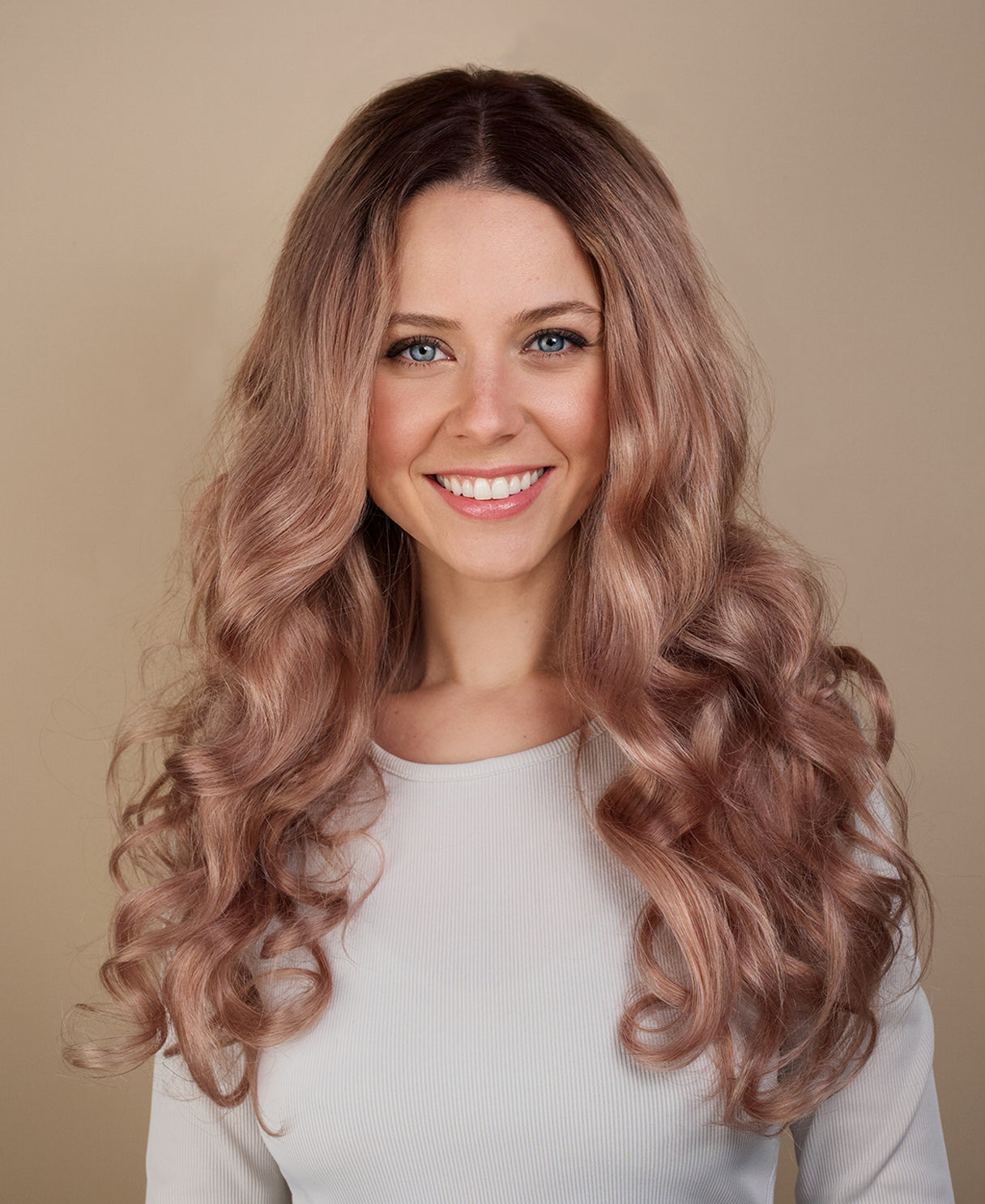Woman with long, wavy, pinkish-brown hair smiling against a beige background