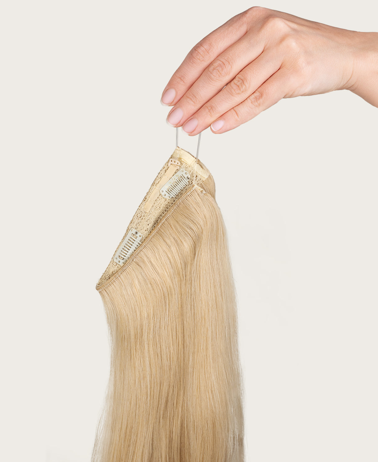 Blonde hair extension held by a hand against a light background