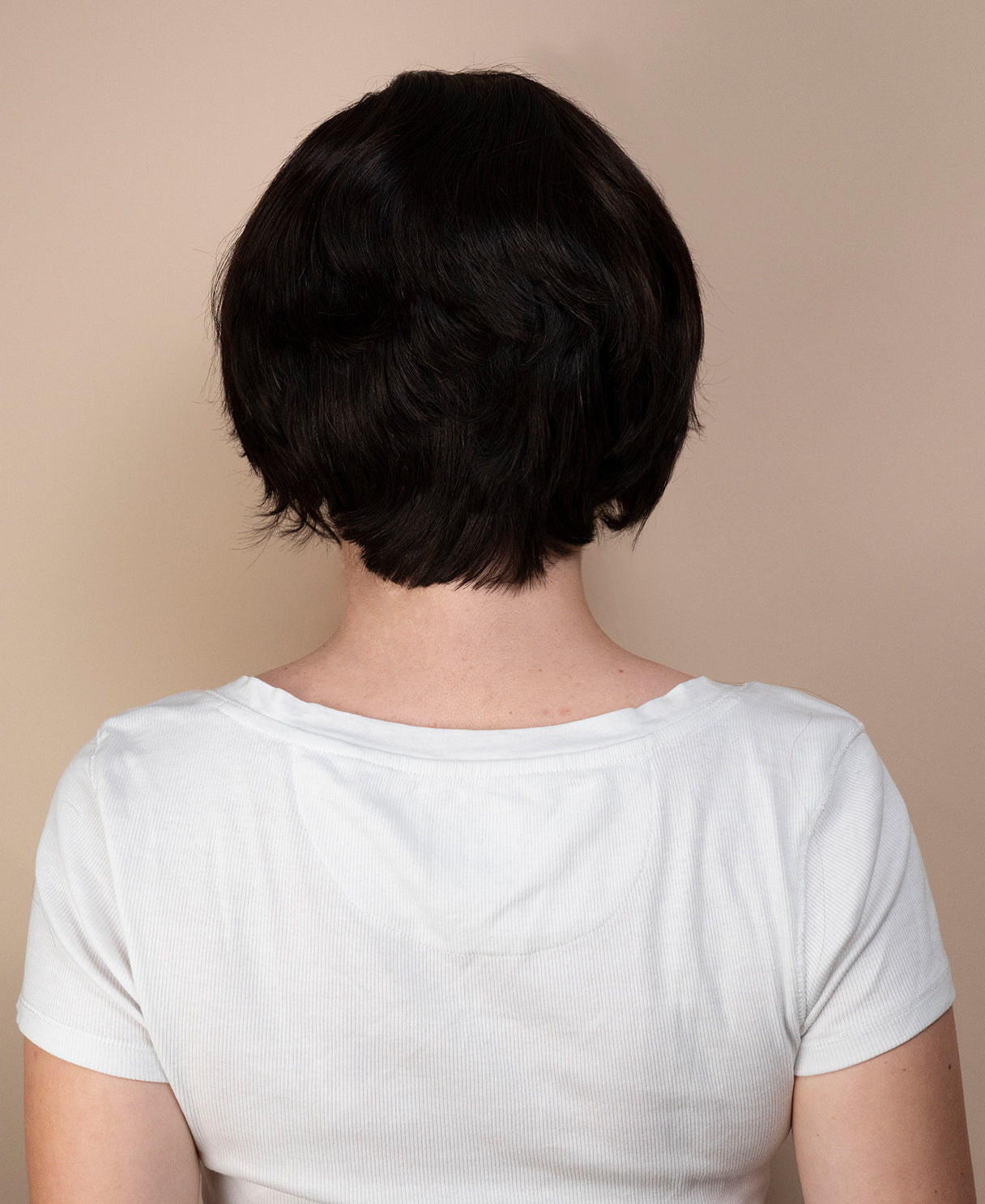 Person with a short black haircut wig wearing a white shirt against a beige background