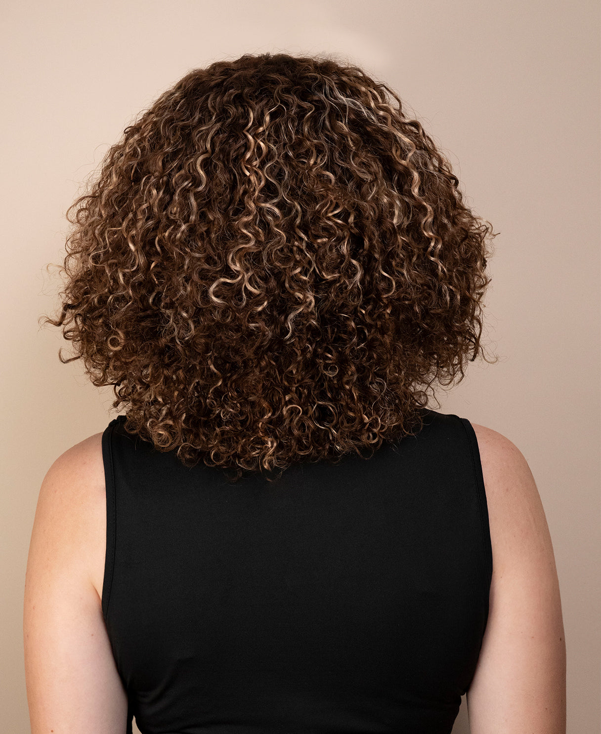 Person with curly hair wearing a black sleeveless top against a beige background