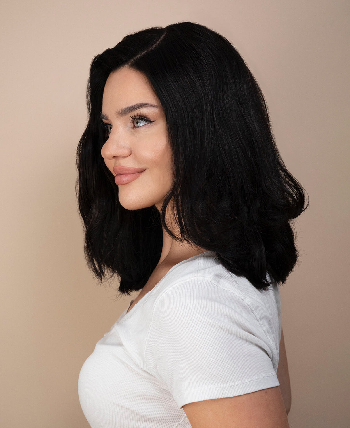 Woman with styled black hair wig wearing a white shirt against a beige background