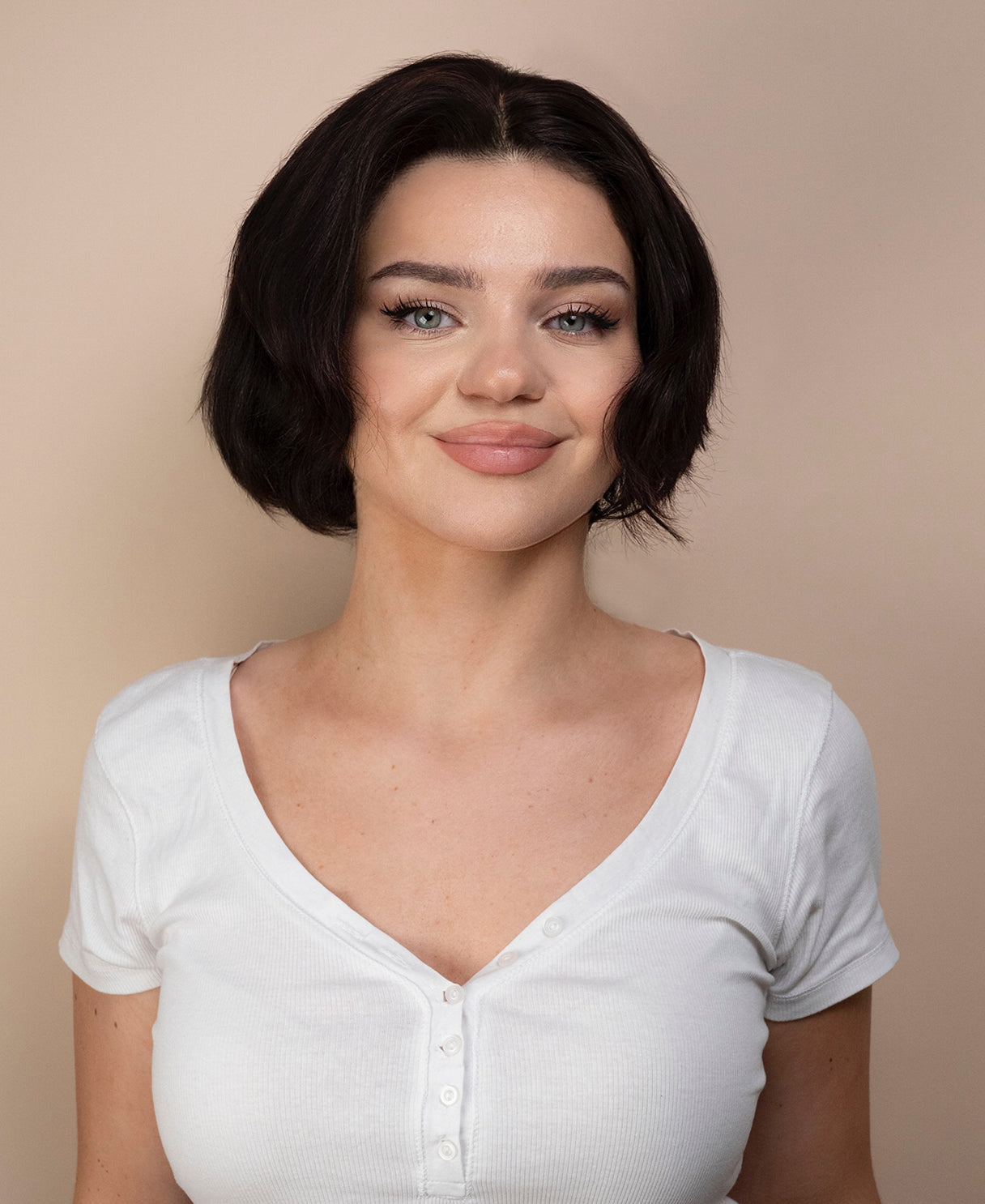 Woman wearing a black hair wig and white shirt against a beige background