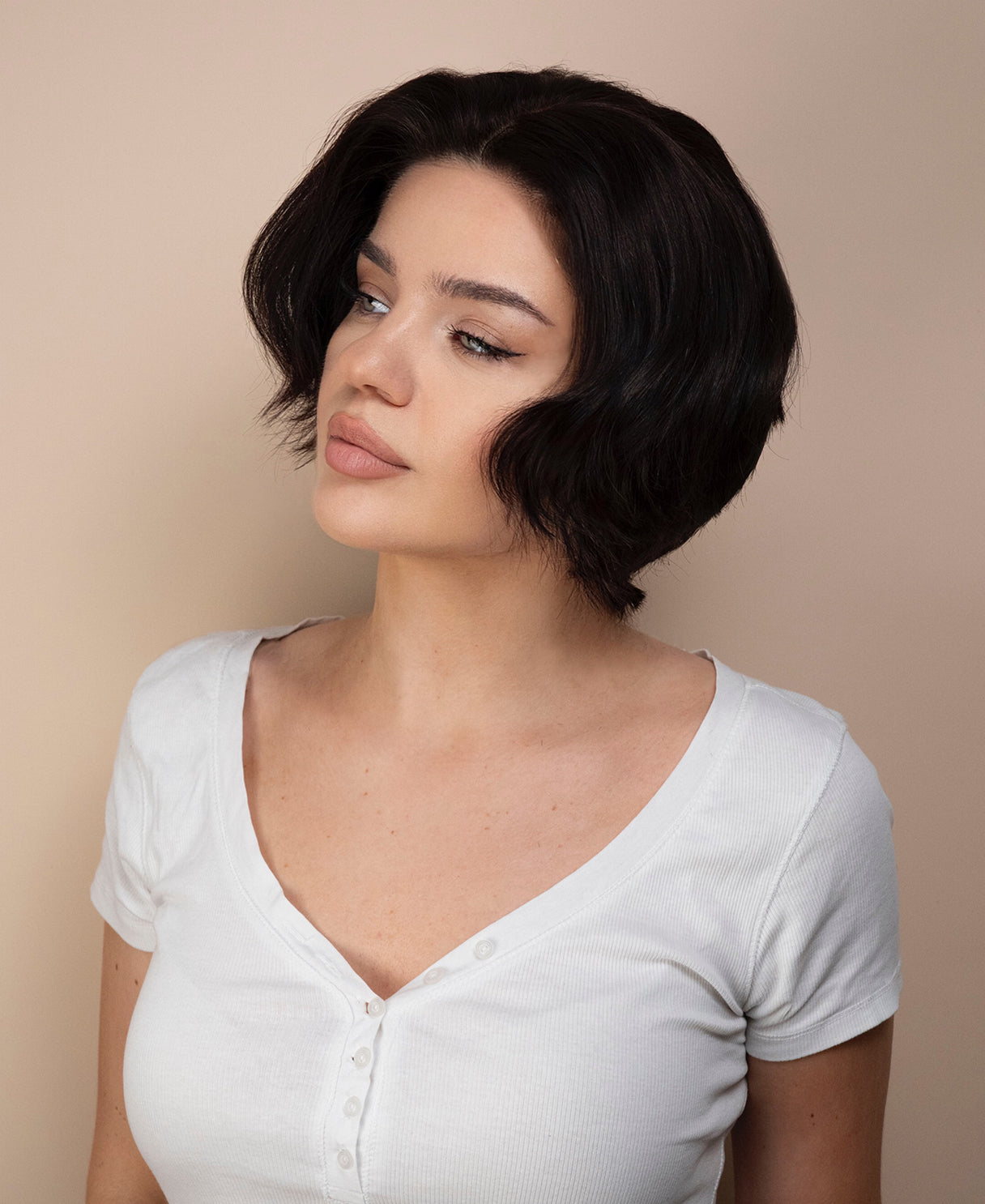 Woman with a short black bob haircut wig wearing a white shirt against a beige background