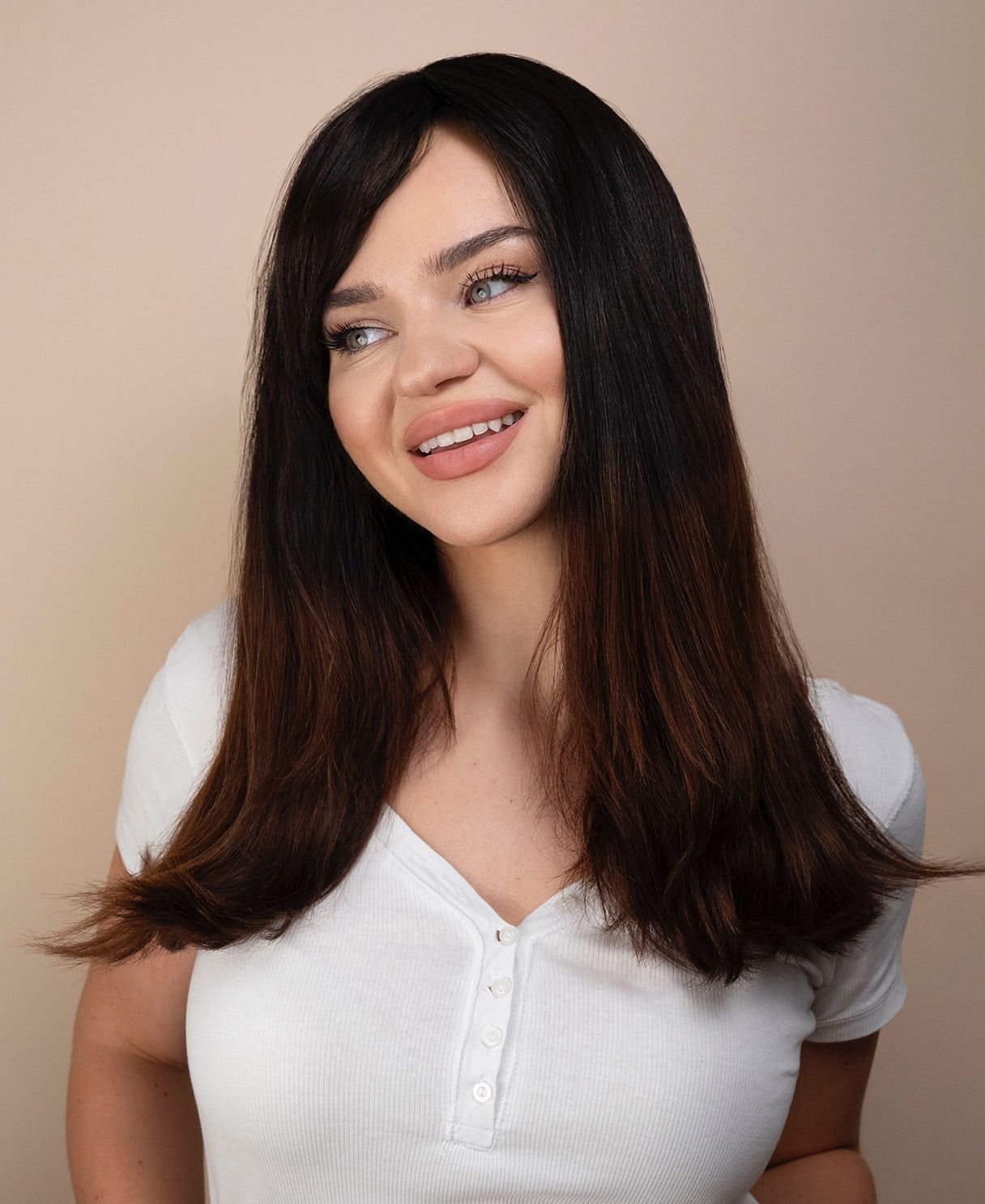 Woman with long dark hair wearing a white shirt against a beige background