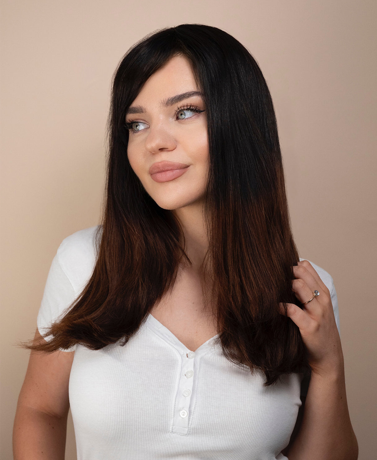 Woman with long dark hair wearing a white shirt against a beige background