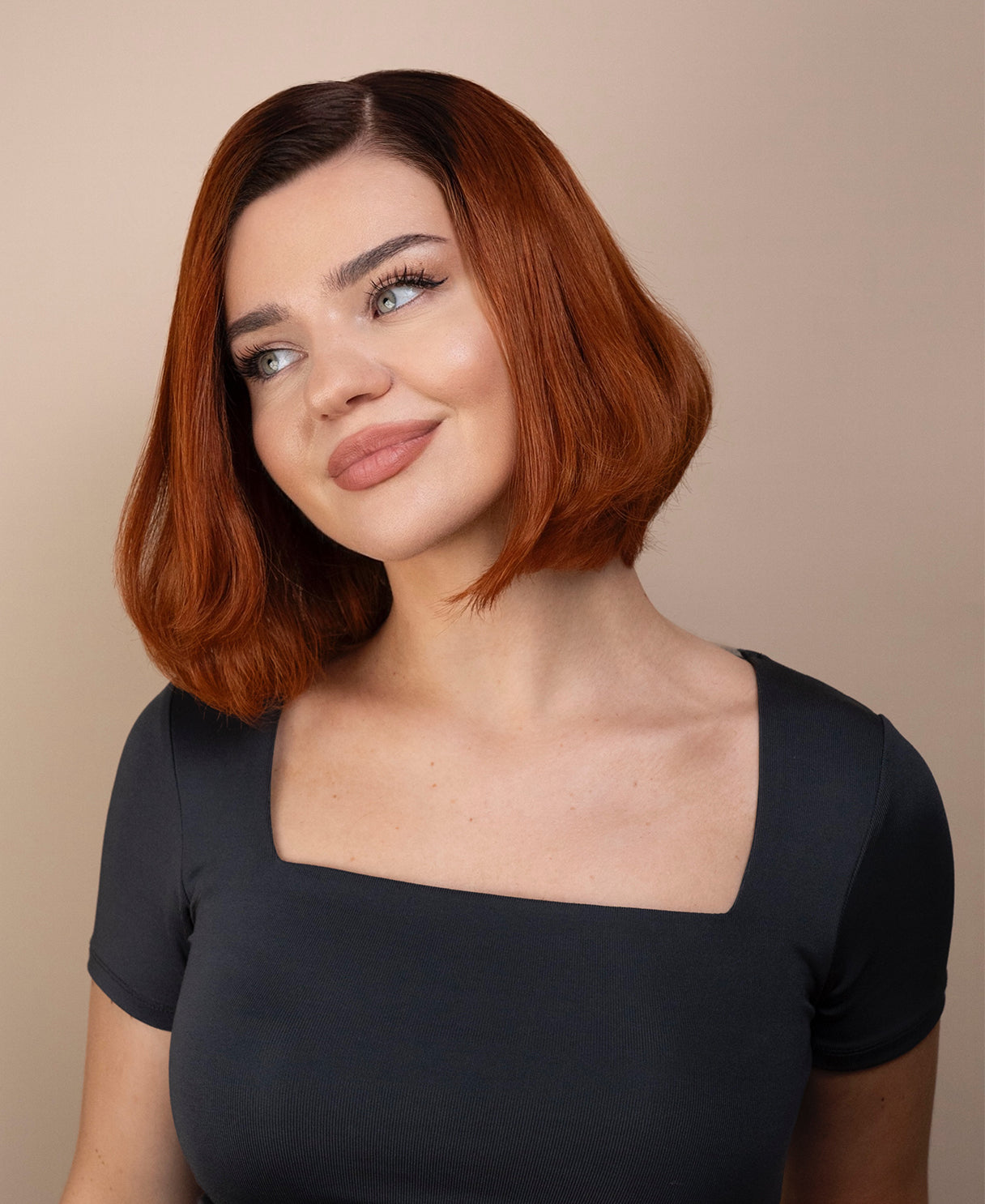Woman with red hair wig wearing a gray top against a beige background