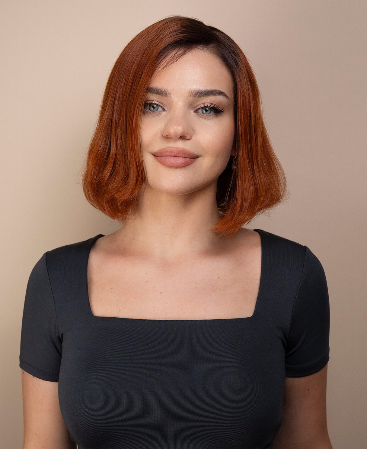 Woman with red hair wig wearing a gray top against a beige background