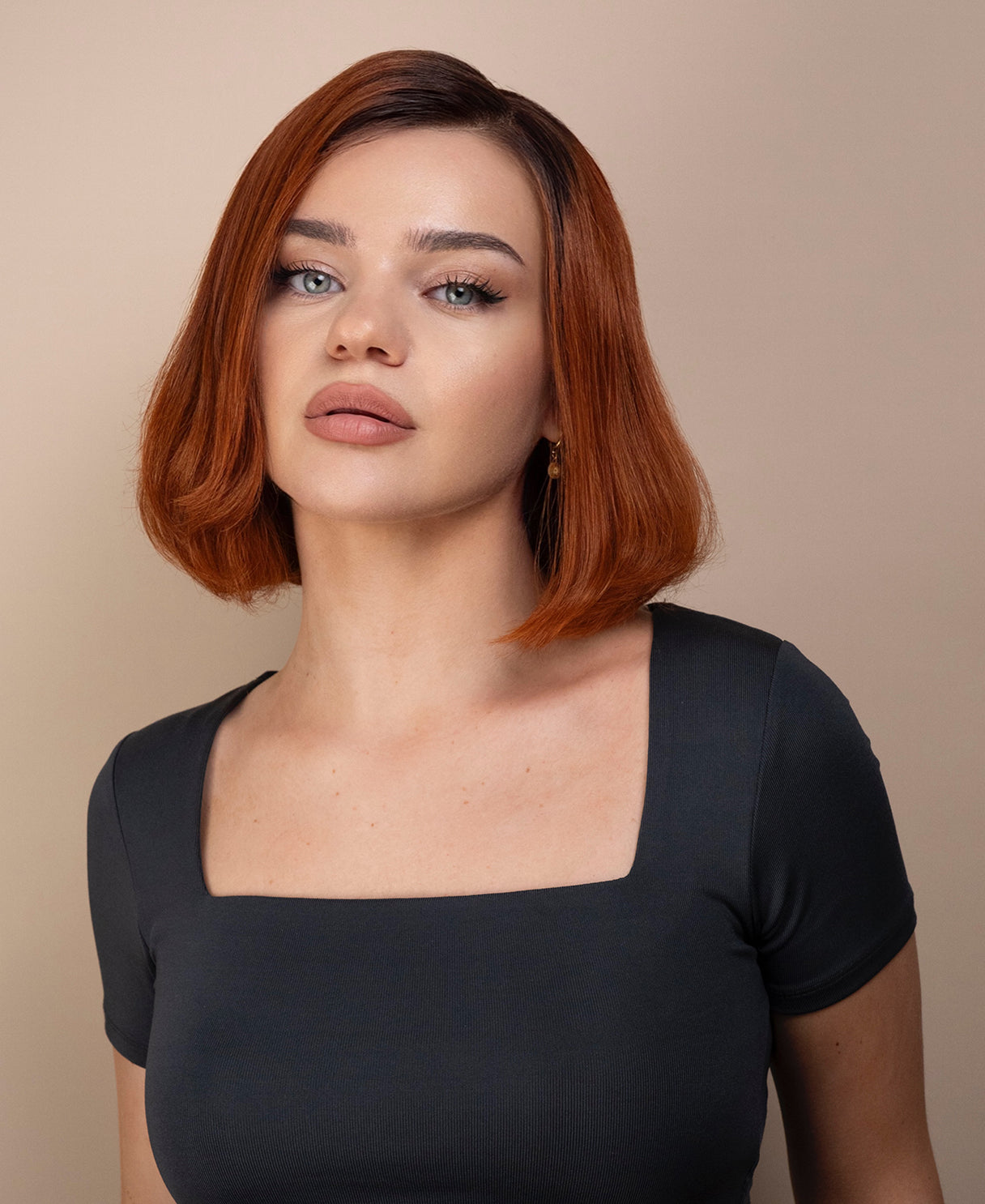 Woman with red hair wig wearing a gray top against a beige background