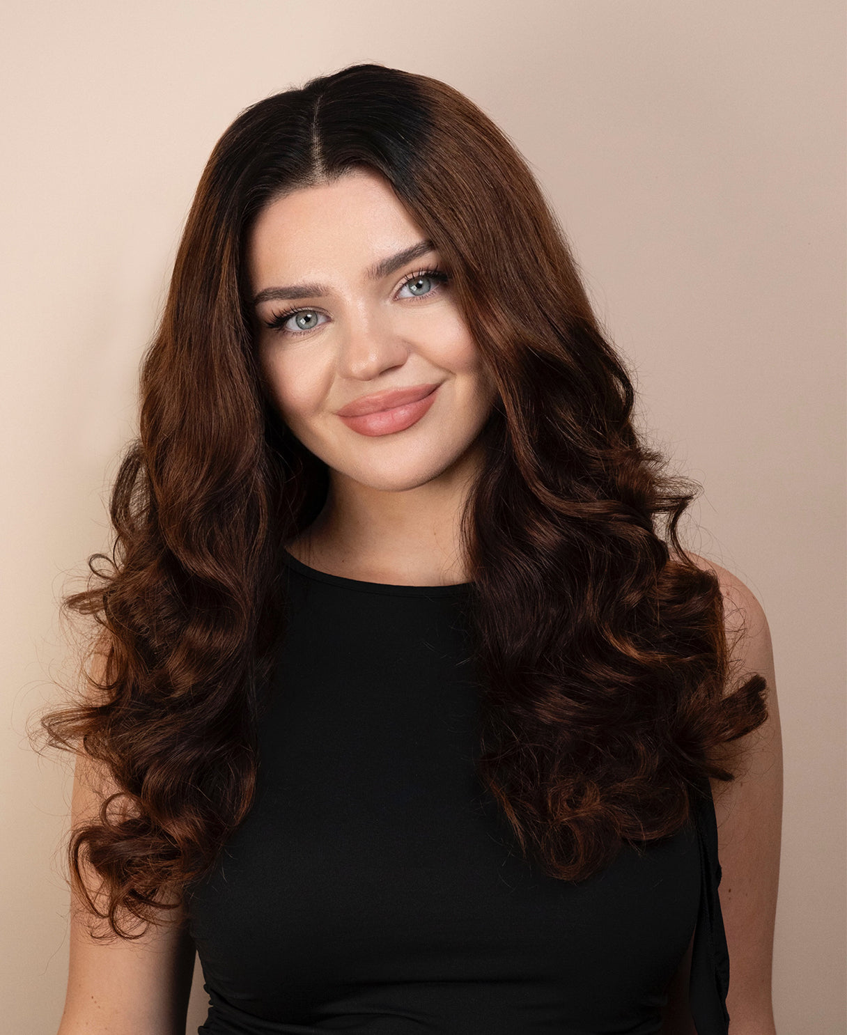 Woman with long, wavy wig hair wearing a black top against a beige background