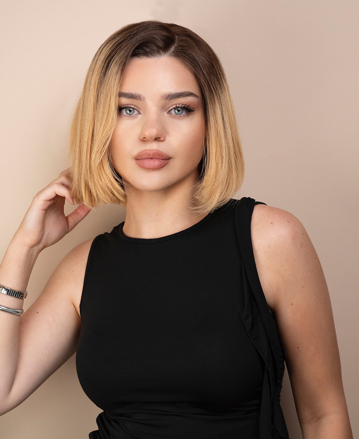 Woman with a stylish blonde haircut wig wearing a black sleeveless top against a beige background