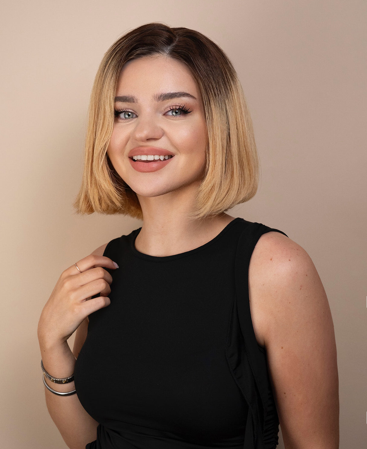 Woman with a stylish blonde haircut wig wearing a black sleeveless top against a beige background