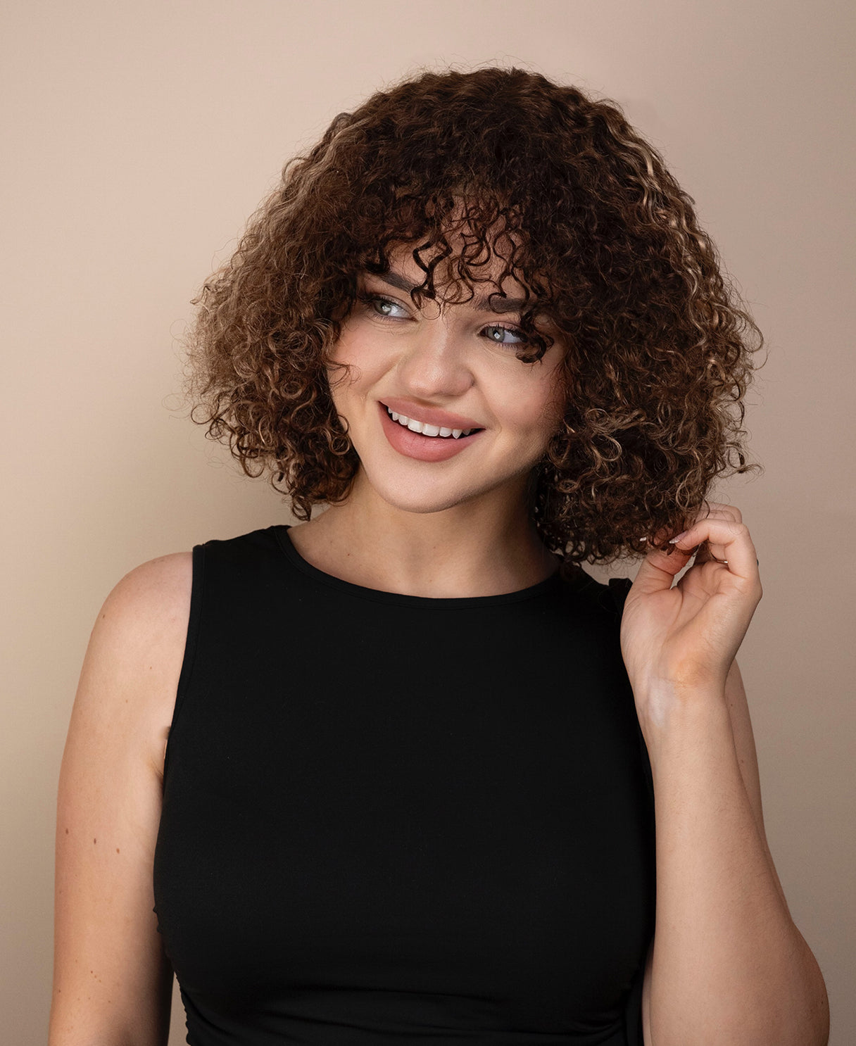 Woman with curly wig wearing a black top against a beige background
