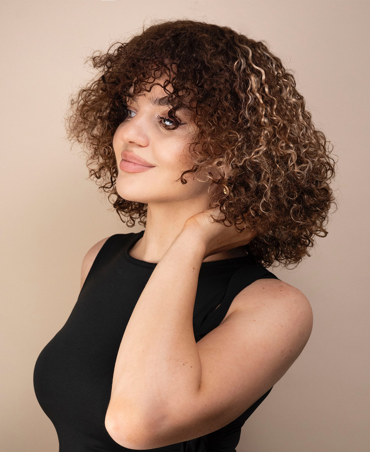 Woman with curly wig wearing a black top against a beige background
