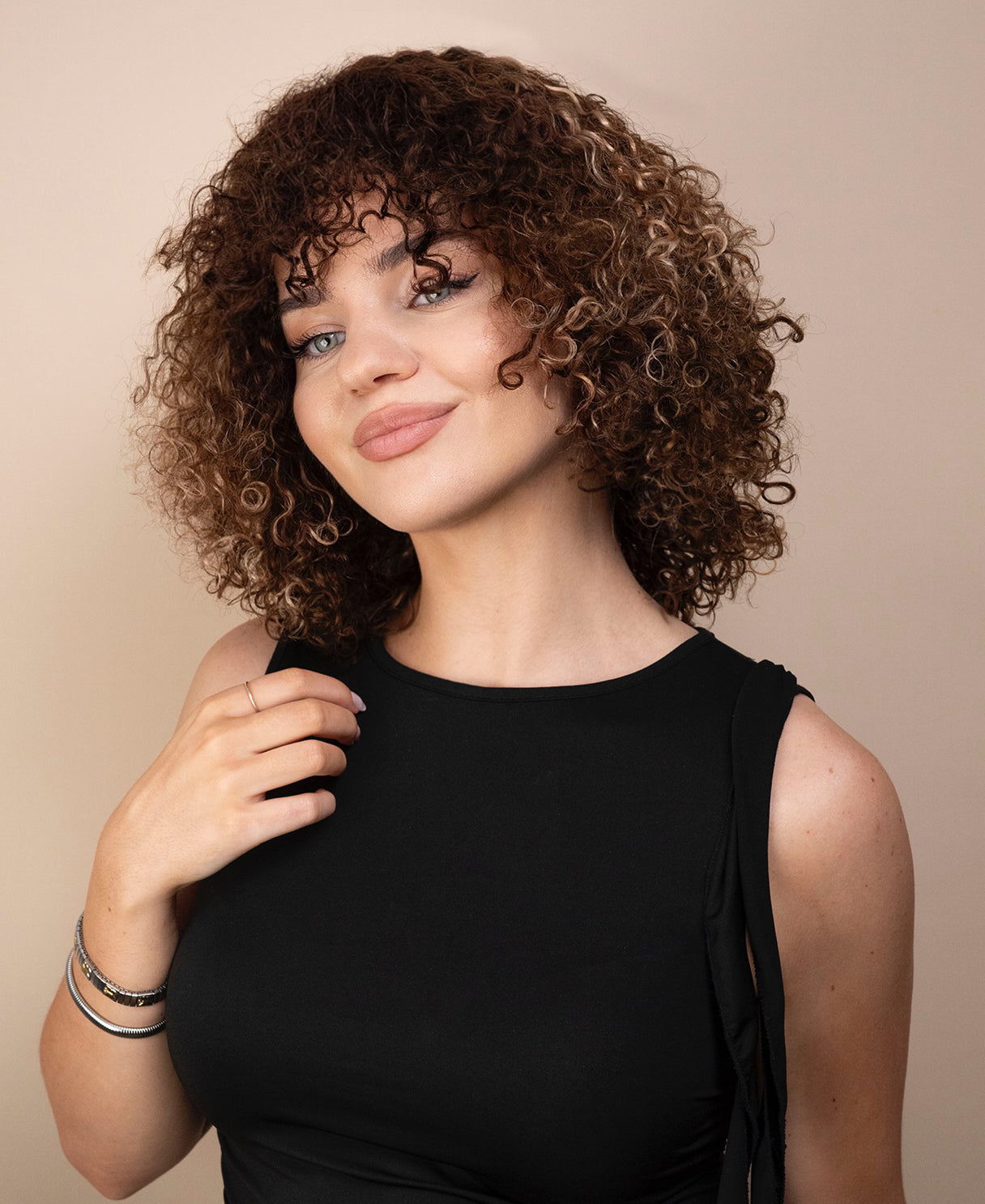 Woman with curly wig wearing a black top against a beige background
