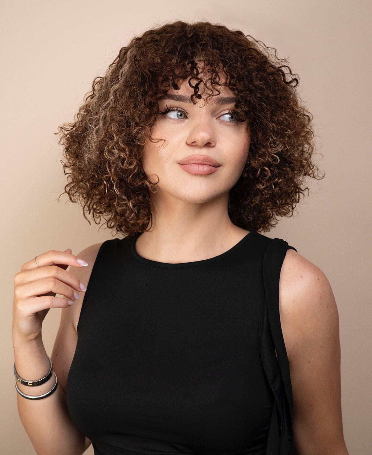 Woman with curly wig wearing a black top against a beige background